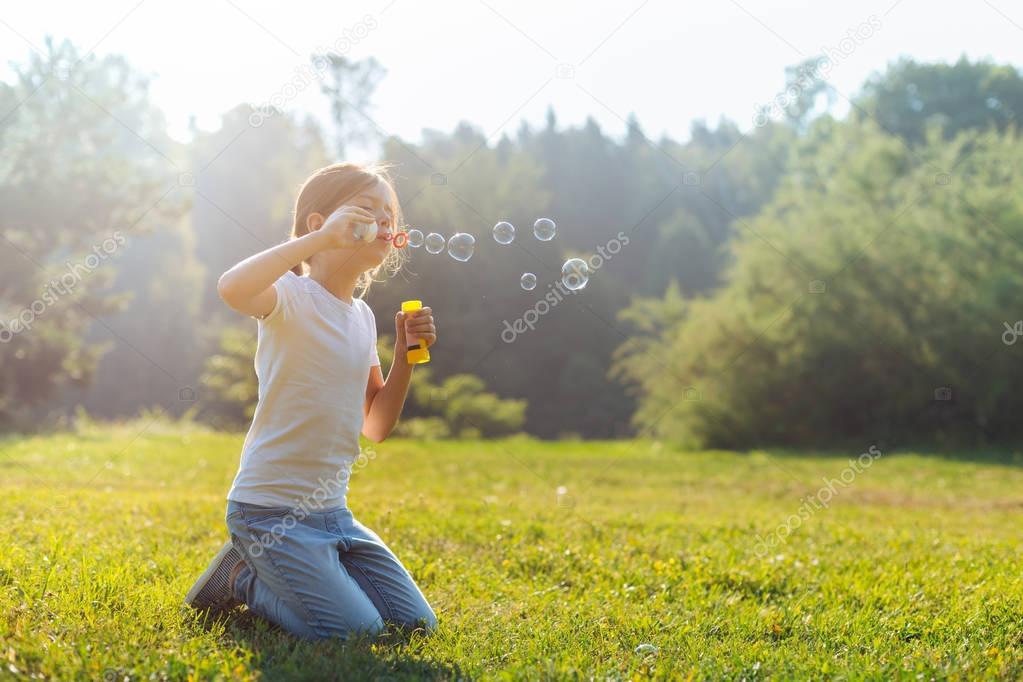 Little girl blowing bubbles while standing on her knees