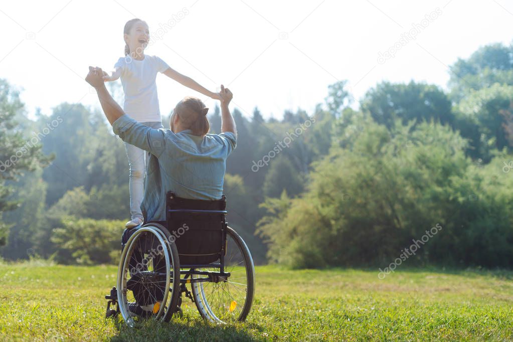 Little girl standing on lap of her father in wheelchair