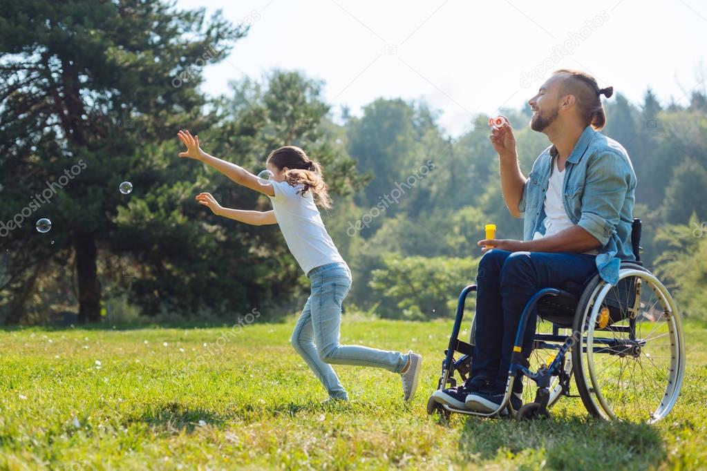 Cheerful disabled father and daughter playing with soap bubbles