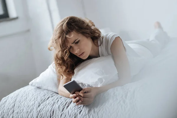 Cheerless young woman looking at her smartphone — Stock Photo, Image