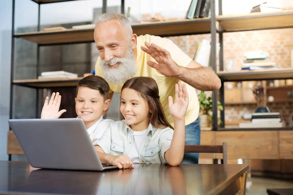 Abuelo y sus nietos saludando a alguien a través de videollamada — Foto de Stock