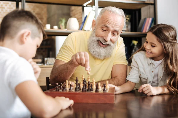 Маленькая девочка смотрит, как ее брат и дедушка играют в шахматы — стоковое фото