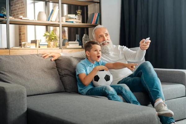 Abuelo aumentando el volumen en la televisión mientras ve el fútbol —  Fotos de Stock