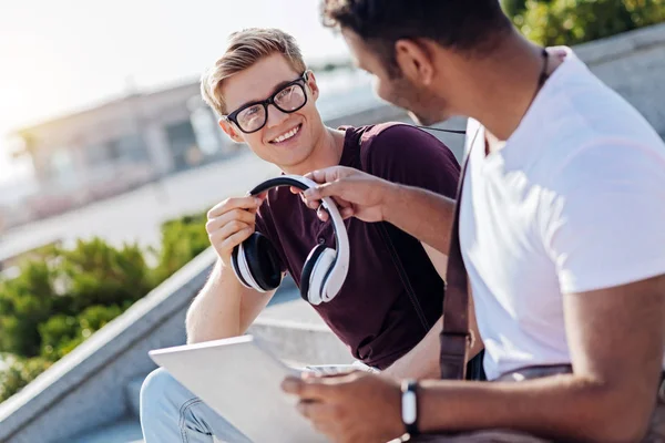 Estudiante positivo tomando auriculares de su amigo —  Fotos de Stock