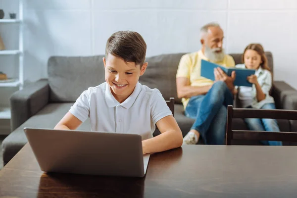 Niño jugando en el ordenador portátil, mientras que la hermana y el abuelo leer libro — Foto de Stock