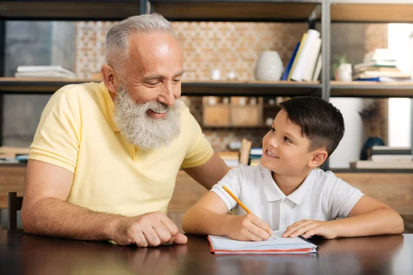 Улыбающийся дедушка помогает своему внуку с математическим заданием — стоковое фото