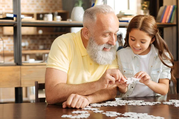 Granddaughter and grandfather trying to join two puzzle pieces — Stock Photo, Image