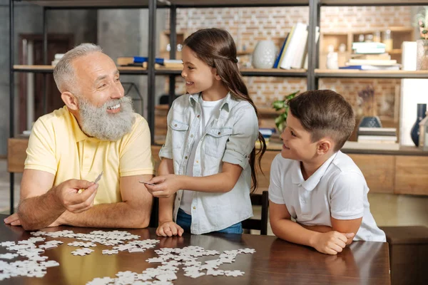 Grandfather and grandchildren assembling jigsaw puzzle altogether — Stock Photo, Image