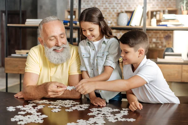 Siblings and their grandfather assembling a jigsaw puzzle — Stock Photo, Image