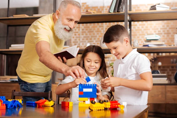 Nonno aiutare i nipoti a costruire una torre con set di costruzione — Foto Stock