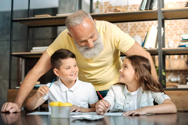 Веселые внуки разговаривают со своим дедушкой во время рисования — стоковое фото