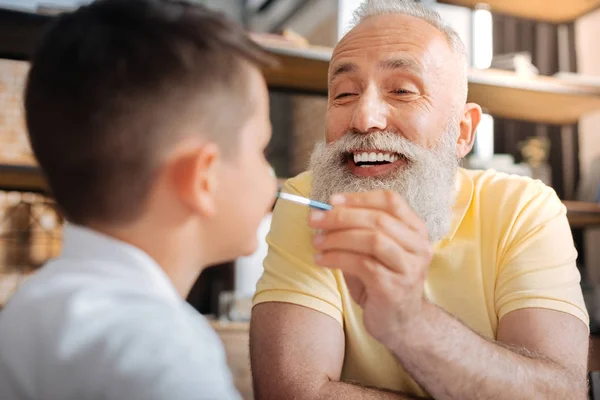 Cheerful senior man putting a paint dot on grandsons nose — Stock Photo, Image