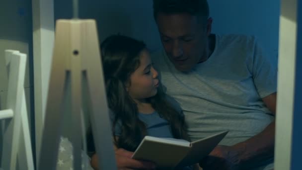 Позитивный заботливый отец читает книгу со своей милой дочерью — стоковое видео
