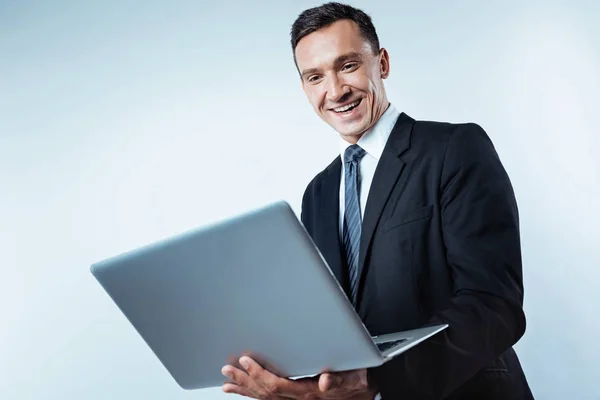 Successful gentleman grinning broadly while looking at laptop — Stock Photo, Image