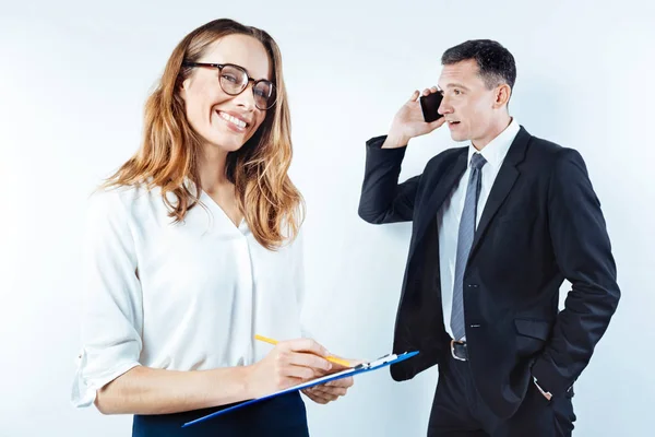 Позитивная женщина делает заметки рядом с коллегой, разговаривающей по телефону — стоковое фото