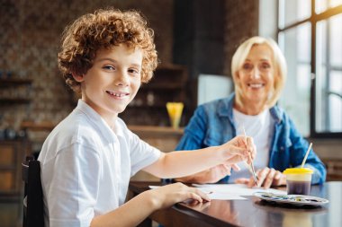 Akıllı kıvırcık saçlı çocuk resim yaparken kamera için poz