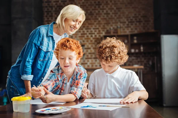 Aufmerksame Oma beim gemeinsamen Malen ihrer Enkel — Stockfoto