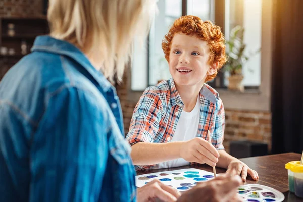 Bonito menino gengibre sorrindo amplamente enquanto olha para a avó — Fotografia de Stock