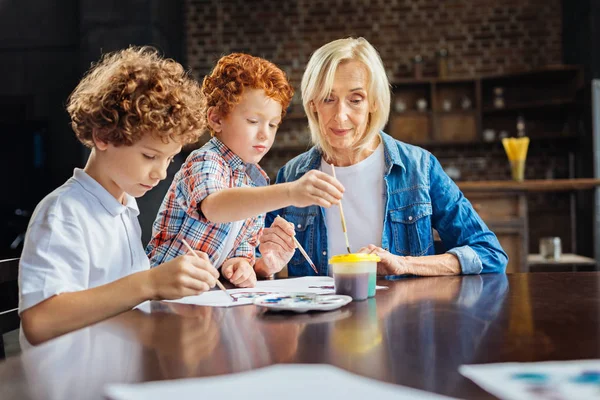 Amar a la abuela enseñando a los nietos a pintar en casa — Foto de Stock