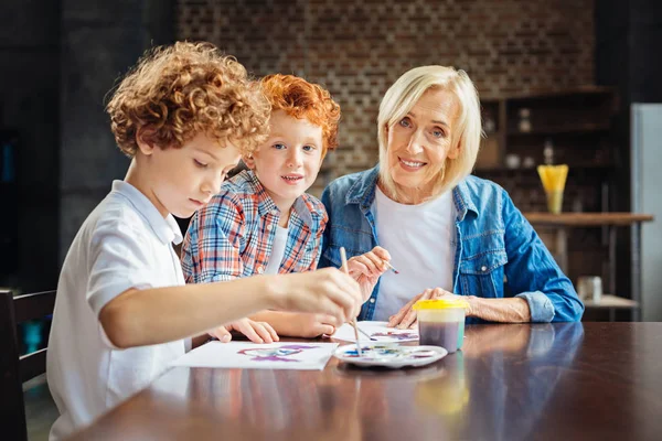 Kind elderly lady painting with grandsons at table — Stock Photo, Image