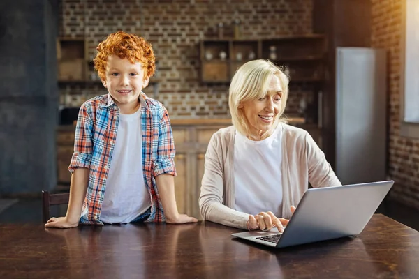 Enfant excité rejoignant sa grand-mère travaillant sur ordinateur portable — Photo