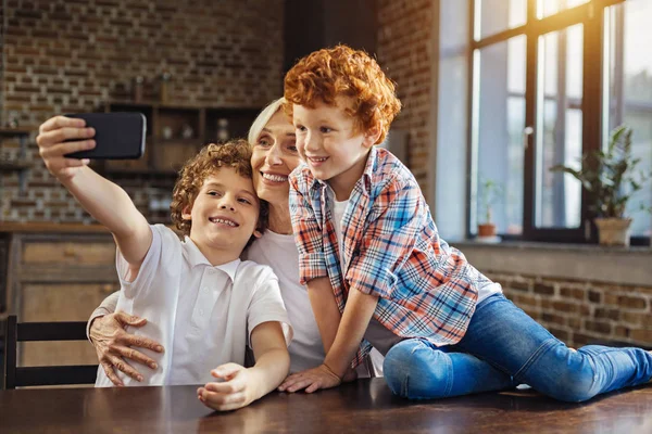 Smiling children and granny taking phones together — Stock Photo, Image