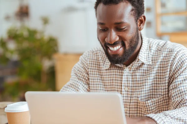 Agradable hombre alegre sonriendo mientras trabaja en el ordenador portátil — Foto de Stock