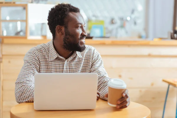 Uomo allegro bere caffè mentre si lavora sul computer portatile — Foto Stock