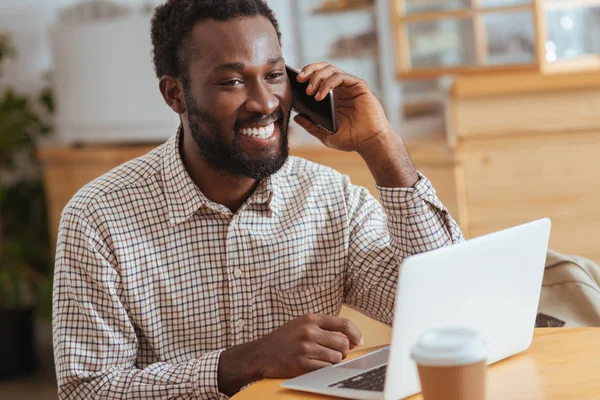 Homem alegre falando ao telefone enquanto trabalhava no café — Fotografia de Stock