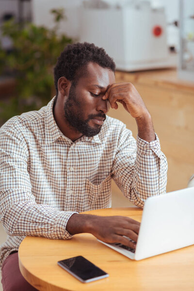 Tired young man working on laptop in cafe