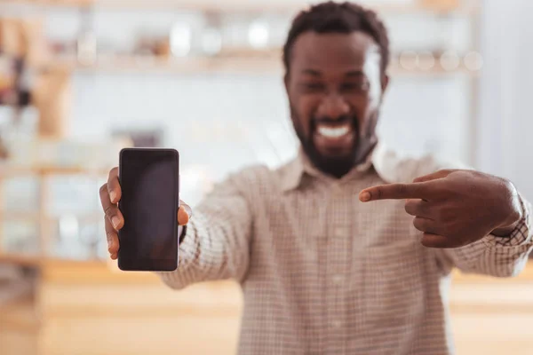 Smiling man pointing at new phone in cafe