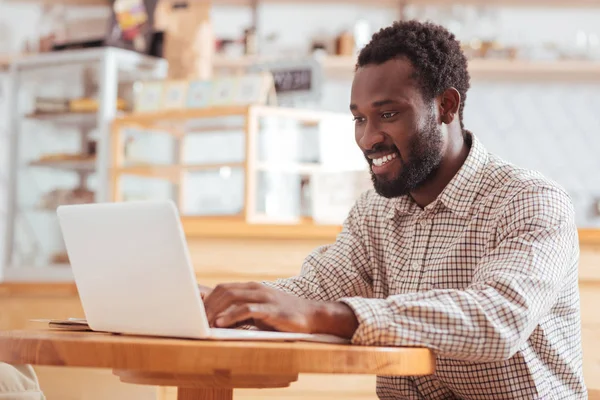 Piacevole giovane uomo che lavora sul computer portatile in caffetteria — Foto Stock