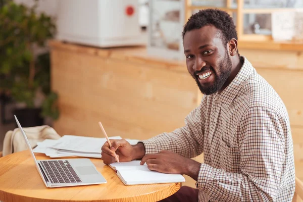 Fröhlicher Mann lächelt, während er im Café Notizen macht — Stockfoto