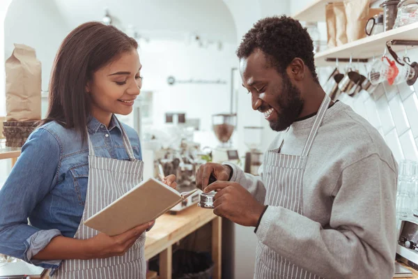 Mulher barista fazendo anotações enquanto seu colega escrutinando portafilter — Fotografia de Stock