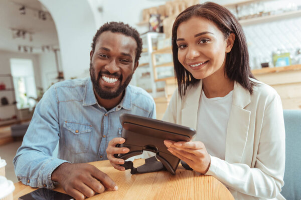 Cheerful best friends posing with VR headset in coffeehouse