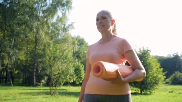 Mujer sosteniendo una esterilla de ejercicio y caminando — Vídeos de Stock