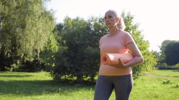 Mujer caminando con una esterilla de ejercicio — Vídeo de stock
