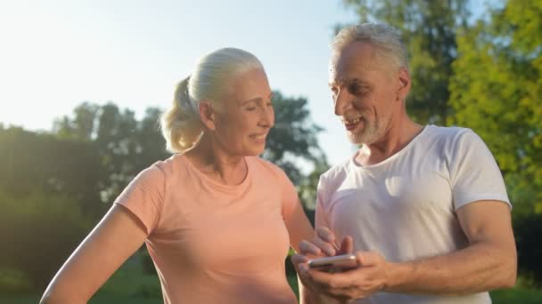 Glada sportiga äldre par med hjälp av smartphone i parken — Stockvideo