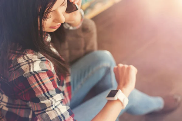 Mujer morena freelancer mirando en reloj de pulsera durante la conversación telefónica — Foto de Stock