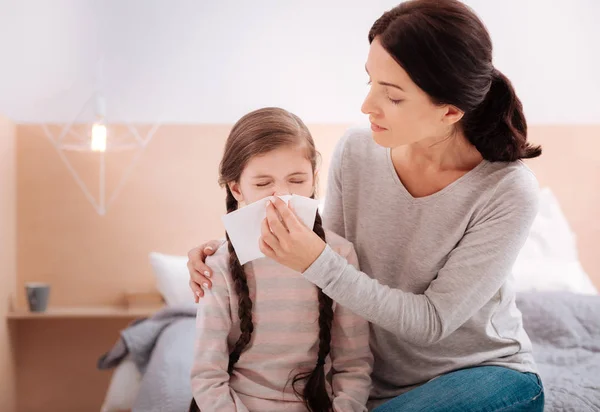 Little girl sneezing while sitting with her mother — Stock Photo, Image