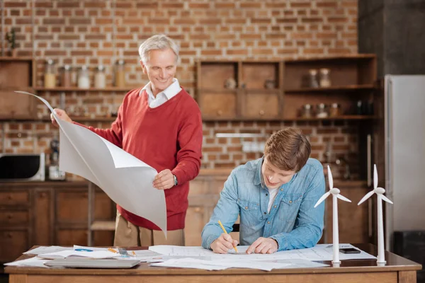 Senior man holding blueprint and watching his colleague draw one — Stock Photo, Image