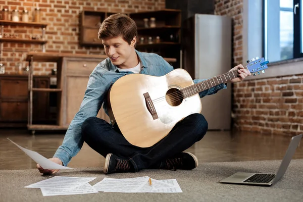 Glimlachende man zittend op de vloer en het lezen van bladmuziek — Stockfoto