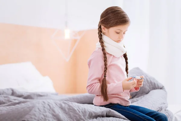 Внимательный ребенок сидит на кровати с термометром — стоковое фото