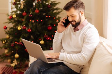 Gülümseyen adam telefonda konuşurken laptop yazarken