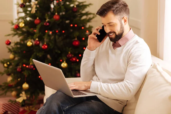Gülümseyen adam telefonda konuşurken laptop yazarken