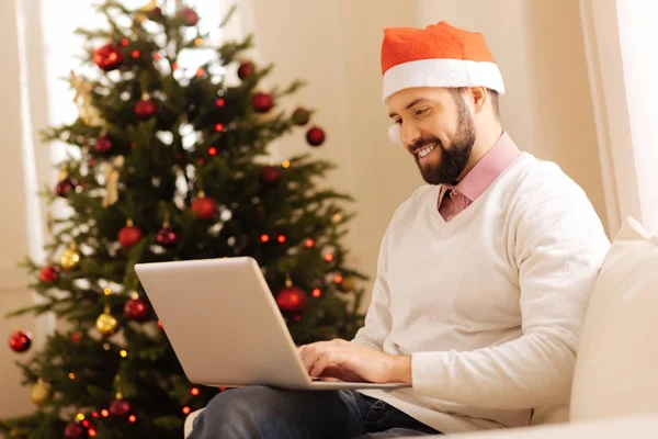 Agréable homme dans le chapeau de Père Noël travaillant sur ordinateur portable — Photo