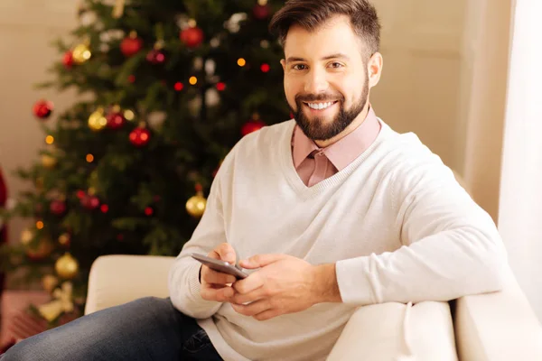 Glimlachende man die zich voordeed op sofa met telefoon in handen — Stockfoto