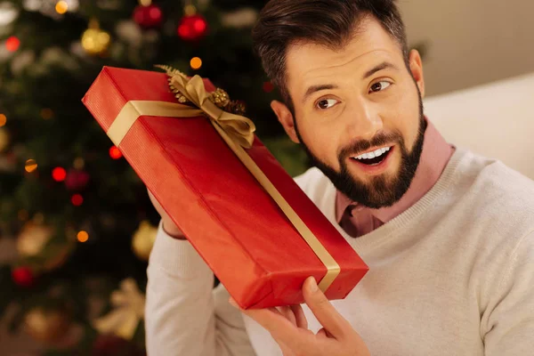 Smiling man wanting to know insides of gift box — Stock Photo, Image