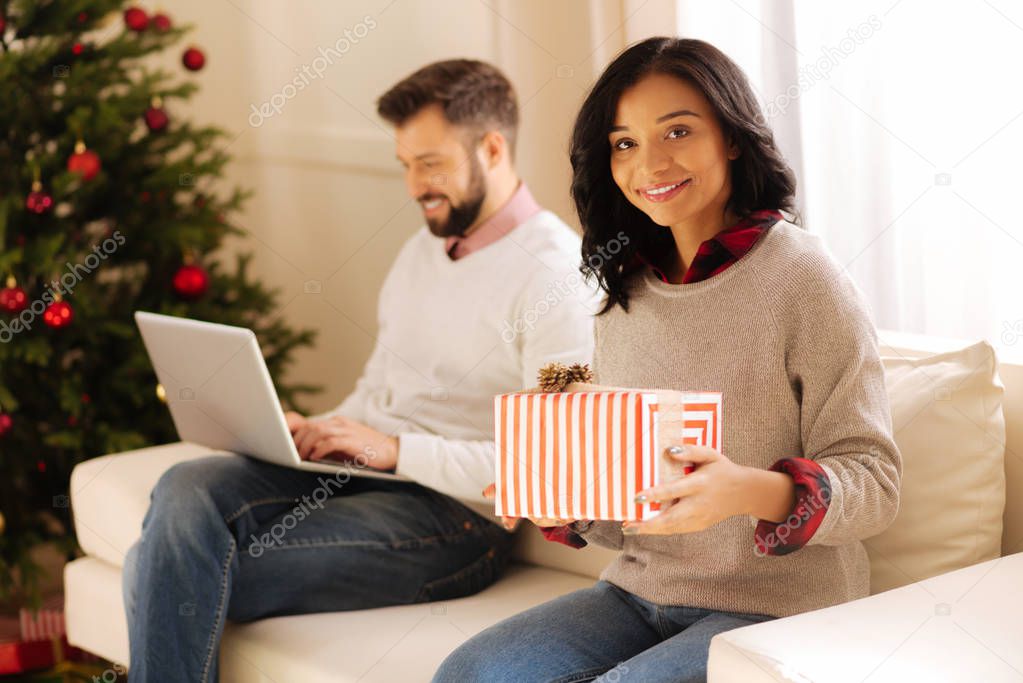 Charming woman posing with gift box on sofa