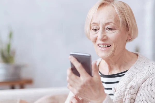 Pretty excited elderly woman texting on phone